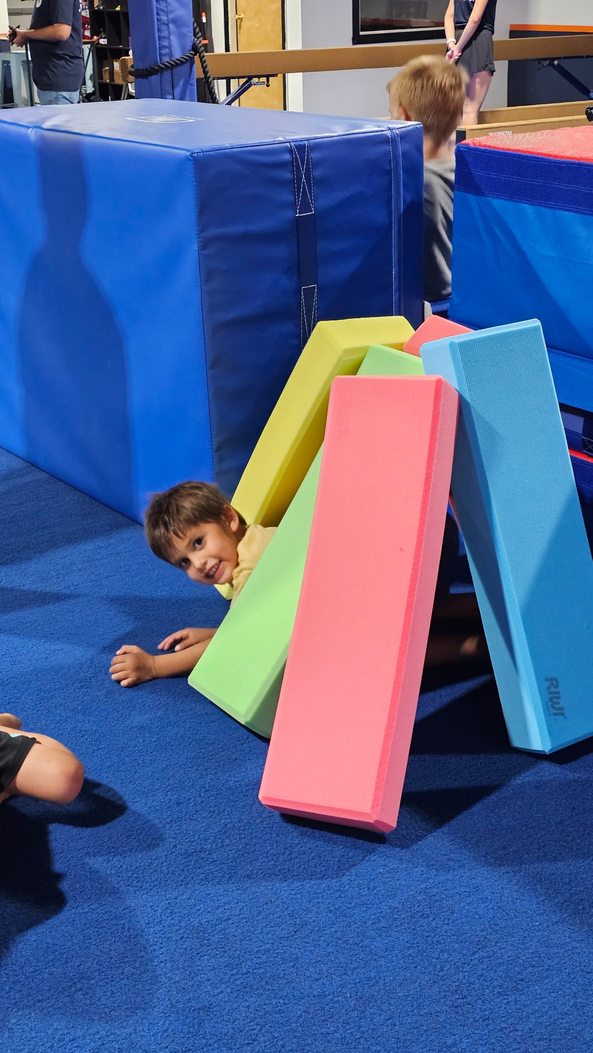 A young boy grinning from behind a fort of foam blocks