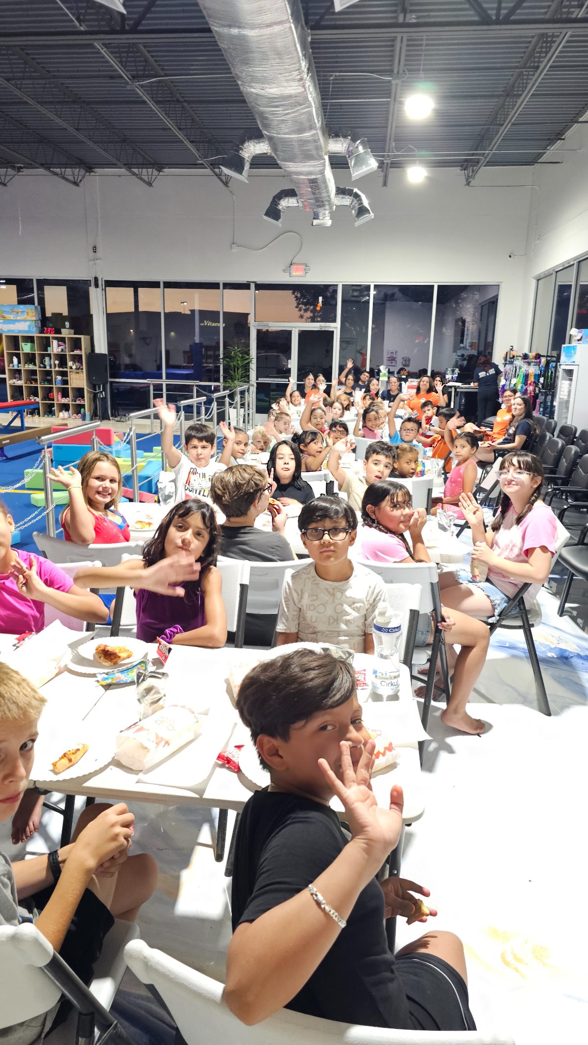 Kids waving from the tables while eating pizza at Kids Night Out